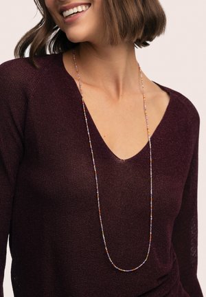 Collar largo de cuentas con cuentas multicolores, sobre un suéter burdeos oscuro con diseño de cuello en V. Textura suave, ligera.