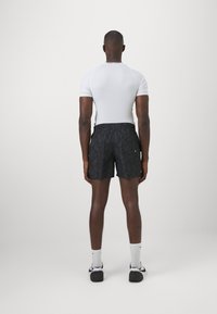 Compleu sportiv masculin format dintr-o bluză albă ajustată și pantaloni scurți negri cu imprimeu geometric, asortați cu șosete albe și adidași negri.