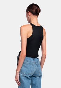 Top de tirantes negro sin mangas con una textura suave, combinado con jeans de tiro alto en azul claro que cuentan con bolsillos traseros y un corte relajado.