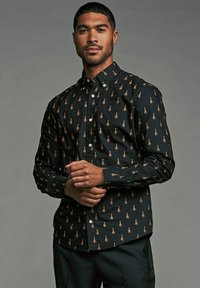 Chemise noire à boutons avec un motif d'arbres dans des tons dorés, dotée d'un col classique et de manches longues, fabriquée dans un tissu texturé.