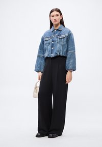 Gombos farmerdzseki, két mellzsebbel és puffos ujjakkal; fekete bő szárú nadrággal és kis bézs kézitáskával párosítva.