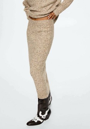 Osoba ubrana w beżowy prążkowany zestaw z dzianiny, składający się z spódnicy i swetra, do którego dobrano czarno-białe skórzane buty w stylu western.