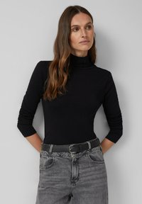 Zwarte lange mouwen turtleneck-top met een nauwsluitend ontwerp, gemaakt van zacht materiaal. Gecombineerd met hoge, vervaagde zwarte jeans en een zwarte riem.