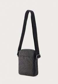 Schwarze Leder-Umhängetasche mit glatter Textur, ausgestattet mit Reißverschluss, verstellbarem Riemen und geprägt dargestelltem Logodetail.