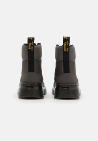 Paire de bottines noires en cuir et tissu avec semelles épaisses et coutures jaunes, vues de dos sur un fond blanc.