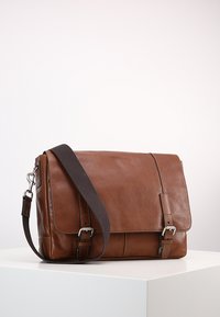 Sac messager en cuir marron avec une fermeture à rabat, une sangle marron réglable, des ferrures en argent et des accents de boucle sur le devant.