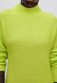 Pull en tricot vert lime vif avec un col montant, des manches amples et un tissu texturé présentant un motif de mailles fines.