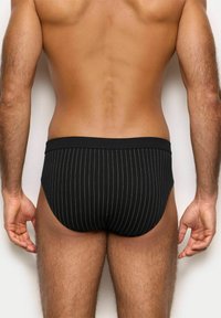 Sorte stribede briefs med en ensfarvet talje, der har fine lodrette striber og en tætsiddende pasform, vist fra bagsiden.
