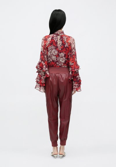 Piros virágos muszlin blúz fodros ujjakkal, bordó bőrdzoggerrel, amely elasztikus mandzsettákkal és oldalzsebekkel rendelkezik.