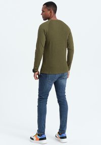 Vihreä oliivi pitkähihaisuus ribbipaita, slim fit -design, yhdistetty sinisiin farkkuihin ja monivärisiin lenkkareihin, joissa on paksu pohja.