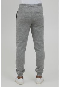 Gray, brushed fabric joggers with elastic waistband, tapered cuffs, side pockets, and one rear pocket. White sneakers paired with the joggers.