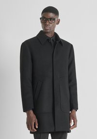 Cappotto in misto lana nero con colletto a punta, due tasche frontali e una silhouette snella. Presenta una chiusura con bottoni e un tessuto testurizzato.