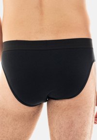 Schwarze Baumwollslips mit einer glatten Textur, ausgestattet mit einem breiten elastischen Bund und einer engen Passform, die die Körperform betont.