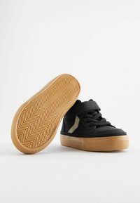 Svarta högklackade sneakers med en strukturerad gummisula, som har svarta skosnören, ett kardborreband och en ljusfärgad sidodekor.