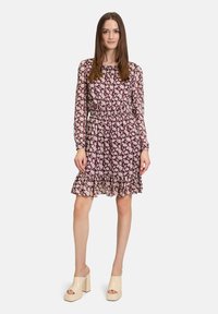 Weinrotes Blumenkleid mit langen Ärmeln, elastischem Bund und gerafftem Saum. Fließender Stoff mit strukturiertem Muster. Kombiniert mit cremigen Blockabsatzschuhen.