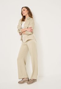 Beige satijnen shirt en wijdvallende broek outfit. Shirt met kraag en knopen, losse pasvorm. Schoenen hebben decoratieve hardware en een gestructureerde afwerking.