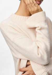 Jasnoróżowy sweter z prążkowanej dzianiny z wysokim kołnierzem i długimi rękawami, o miękkim, teksturowanym wykończeniu i luźnym kroju.