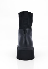 Botas negras hasta el tobillo con un acabado de cuero liso, un cuello de tela acanalada y una suela de goma texturizada, que presentan un diseño robusto y un hardware minimalista.