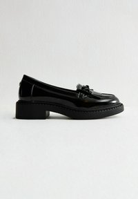 Chaussures en cuir verni noir avec un bout arrondi, un petit talon bloc et un détail de frange décorative sur le dessus. Semelle en caoutchouc texturé.