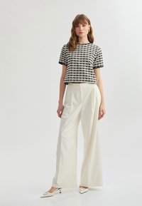 Sort og hvid ternet cropped top med kortærmer, parret med elfenbenfarvede brede bukser og spidse hvide hæle.