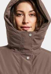 Bruine geïsoleerde jas met een hoge kraag en grote capuchon, voorzien van een drukknoopsluiting en een zachte, matte textuur.