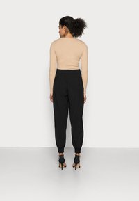 Beige ribbad långärmad topp i kombination med svarta avsmalnande joggers med elastiska muddar och svarta högklackade skor. Släta texturer är synliga.