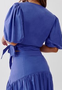 Abito blu con maniche a sbuffo, vita annodata e gonna a più strati. Tessuto liscio e design semplice con un colore uniforme.
