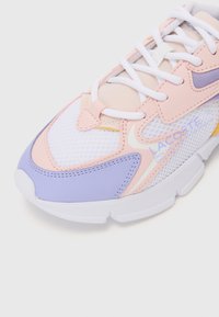 Sapatilhas Lacoste com uma combinação de materiais em malha e lisos, predominantemente brancas, com detalhes em rosa claro e lavanda, e atacadores brancos.