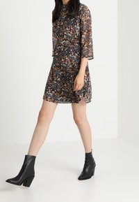 Abito floreale nero in tessuto traslucido, con maniche a tre quarti e una vestibilità ampia. Abbinato a stivaletti neri con tacco.