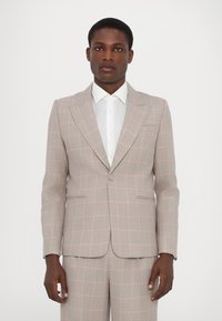 Šviesiai pilkas kostiumas su rožinėmis languotomis detalėmis, turintis užapvalintus atlapus, dvi priekinės kišenės ir dviejų mygtukų užsegimą, derinamas su baltu marškiniai.