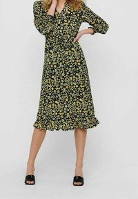 Vestido midi floral en negro con flores amarillas y blancas. Presenta mangas tres cuartos y un dobladillo con volantes. Textura de tela suave.