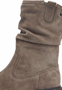 Bottine en suède marron avec un design décontracté, texture lisse et couture contrastante. Elle possède une boucle en haut pour un enfilage facile.