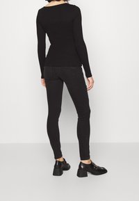 Svart långärmad topp med båturringning, kombinerad med svarta smala jeans och svarta klackskor med blockklackar, sedd bakifrån.