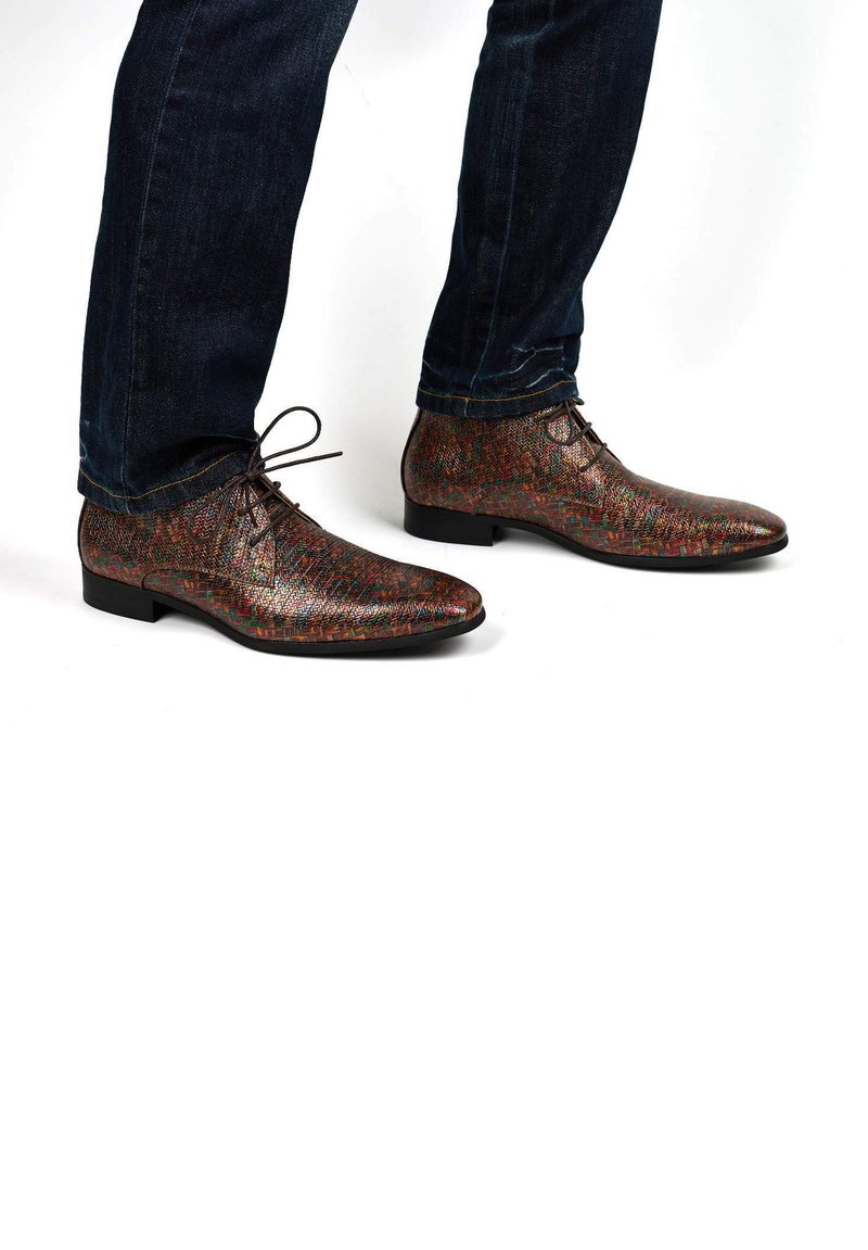 Bruine leren schoenen met een patroon, een spitse neus, vetersluiting en een lage hak, gedragen met donkerblauwe jeans. Textuur met meerkleurige accenten.