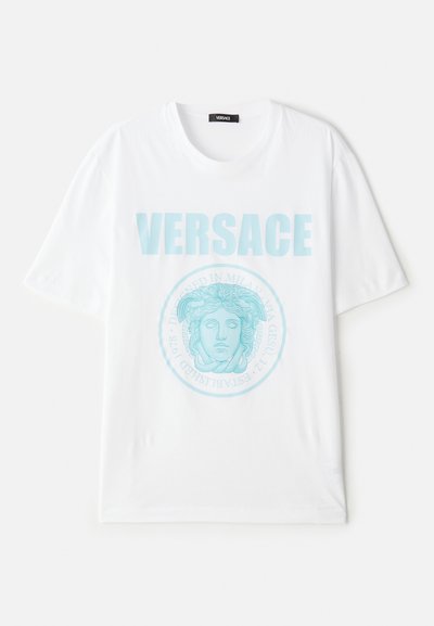 Balta kokvilnas T-kreklā ar apaļu kakla izgriezumu, rotāta ar tirkīza krāsas Medūzas grafiku un izcili izcelto "VERSACE" tekstu.