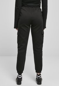 Svarta sweatpants med elastisk midja och muddar vid anklarna, med sidofickor för cargo. Tillverkade av ett mjukt och slätt tyg.