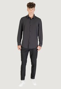 Camicia nera a maniche lunghe con bottoni sul davanti, abbinata a pantaloni neri su misura e sneaker bianche, con una texture di tessuto liscia.