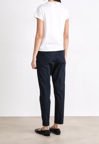 Biała bawełniana koszulka z krótkim rękawem, w zestawieniu z granatowymi spodniami i czarnymi płaskimi butami. Prosty, minimalistyczny wzór bez widocznych wzorów.