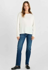 Witte lange mouwen top met een ronde halslijn, gecombineerd met blauwe jeans. De top is glad en heeft een iets losse pasvorm. Schoenen zijn zwarte instappers.