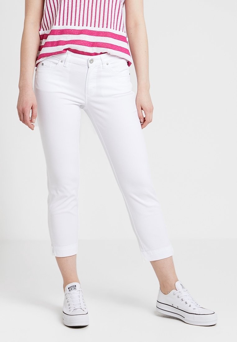 Femme portant un jean blanc court, un haut rayé rouge et blanc, et des baskets basses blanches sur un fond uni.