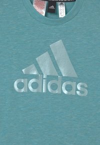 Turquoise T-shirt met korte mouwen van zachte stof, met een groot, metallic zilveren Adidas-logo op de voorkant.
