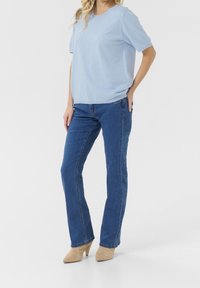 Hellblaues Kurzarmoberteil mit strukturierten Punkten, kombiniert mit dunkelblauen geraden Jeans und beigen spitz zulaufenden Absätzen.