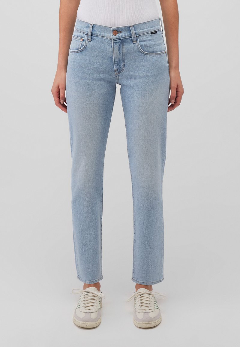 Light blue high-waisted jeans with a straight cut, five pockets, subtle fading, and a button closure. Paired with cream sneakers.