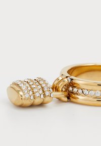 Prsten z zlatne boje s teksturiranim privjescima ukrašenim prozirnim rhinestones, zaobljenog oblika s glatkim završetkom. Vidljivi naglasci sjajnog hardvera.