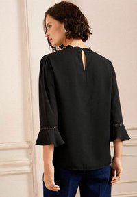 Black blouse with flutter sleeves, a keyhole back, and decorative accents on the cuffs, crafted from lightweight fabric.