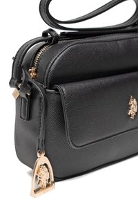 Borsa a tracolla in pelle nera strutturata con chiusura a zip, tasca frontale e dettagli in metallo dorato con un charm con logo.