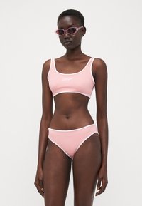Rosa bikinisett med en kort topp og matchende bukser, med hvit kant. Glatt, elastisk stoff med merkevarelogo på toppen.