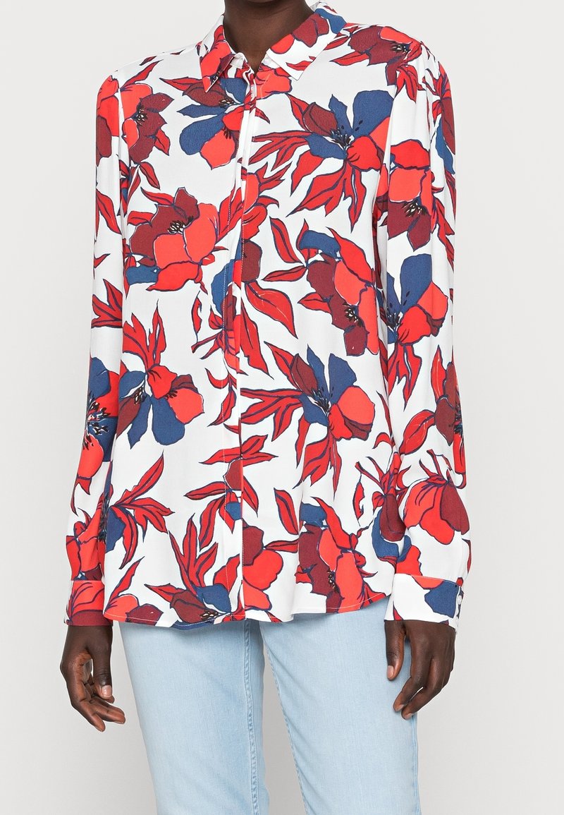 Long-sleeve blouse in lightweight fabric, featuring a white background with red and blue floral patterns, a pointed collar, and button front.