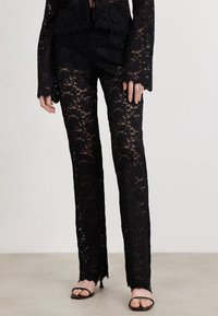 Svart spetsbyxor med intrikata blommönster, med en utsvängd bendesign och scalloped fåll. Kombination med svarta sandaler med remmar.