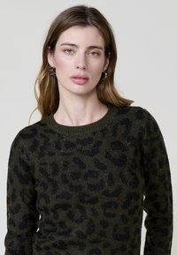 Temno zelena jopica z črnim vzorcem leoparda, teksturirana z subtilnim bleščanjem. Oblikovana s krožnim izrezom, izdelana iz mehkega materiala.